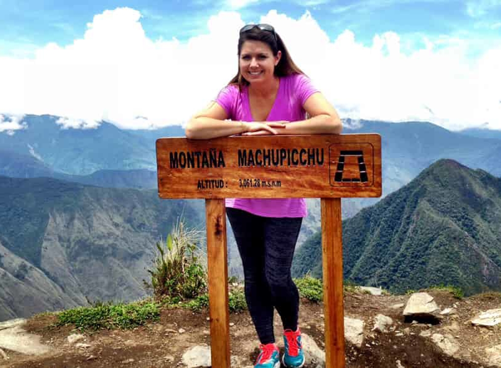 Woman in front of a sign on top of a mountain